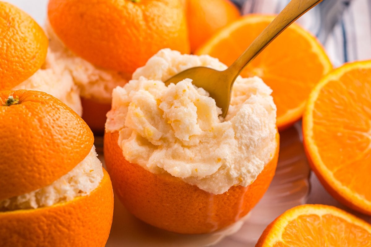 Orange halves filled with creamy orange sorbet, with a spoon scooping some out.