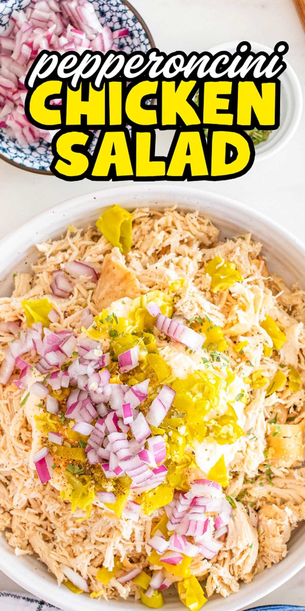 A bowl of pepperoncini chicken salad topped with chopped pepperoncini and red onions, with a bowl of onions nearby.