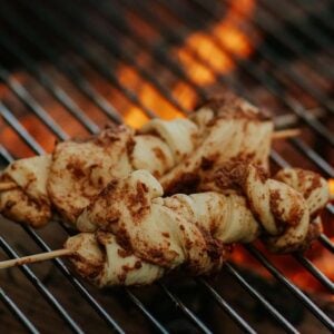 Campfire cinnamon twists being grilled over an open flame on a barbecue grill.