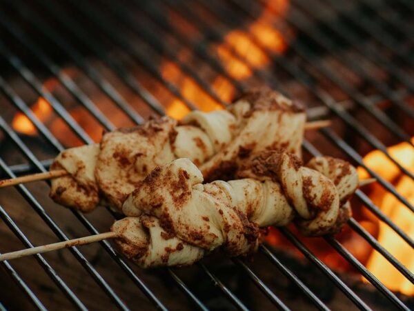 Campfire cinnamon twists being grilled over an open flame on a barbecue grill.