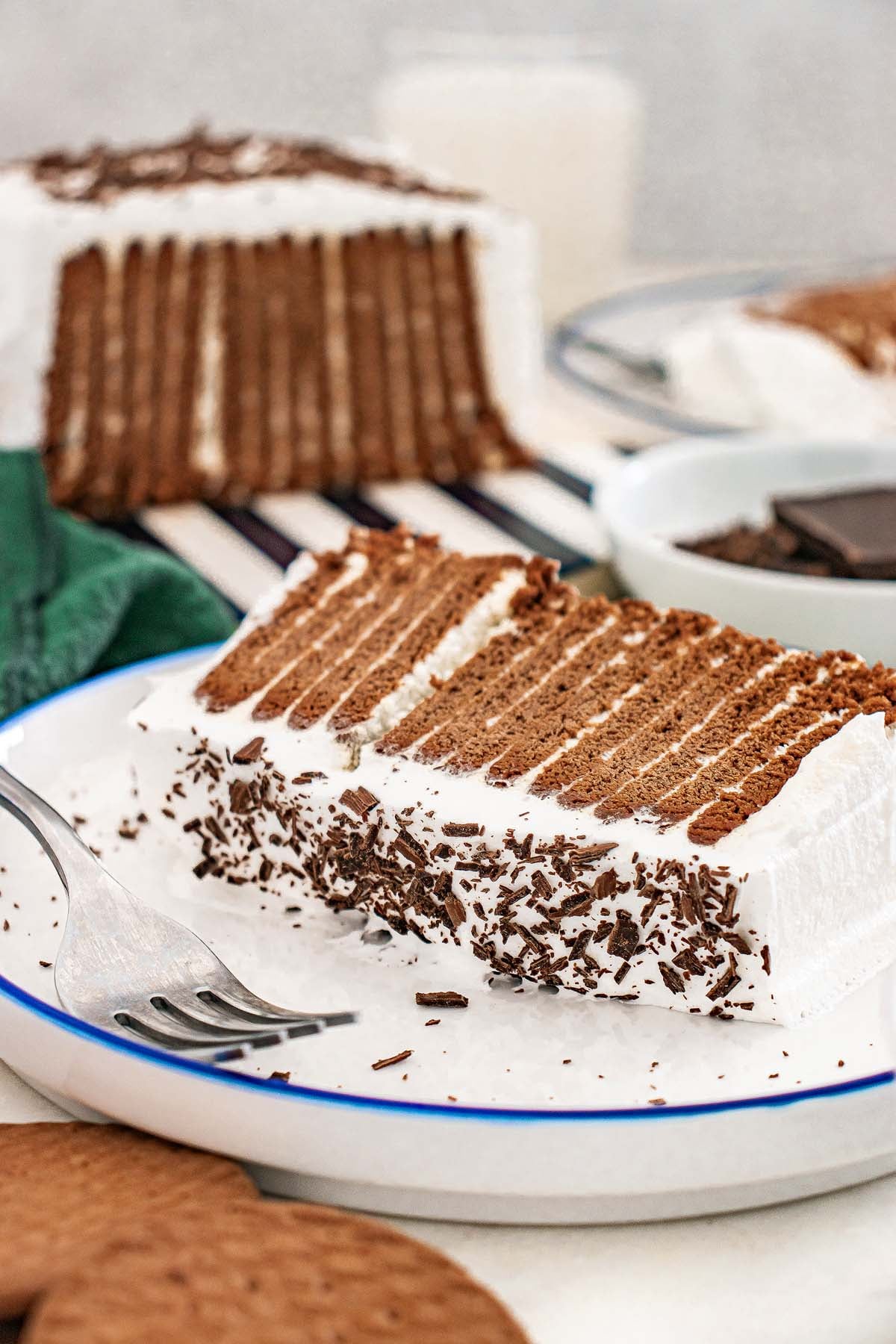 A slice of Chocolate Icebox Cake with whipped cream and chocolate shavings sits on a white plate with a fork.