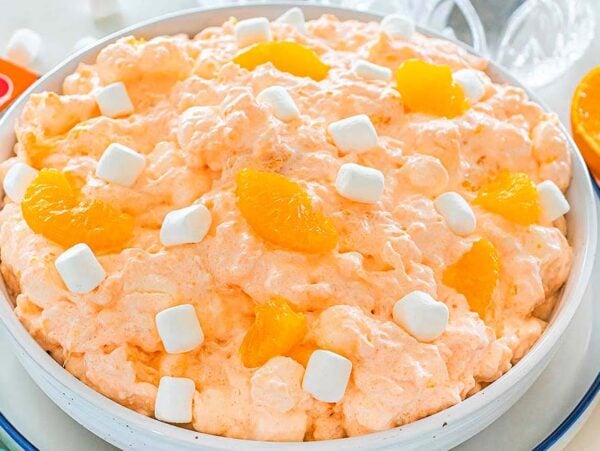 A bowl of Cottage Cheese Jello Salad, featuring orange fluff with mini marshmallows and mandarin orange slices on top.