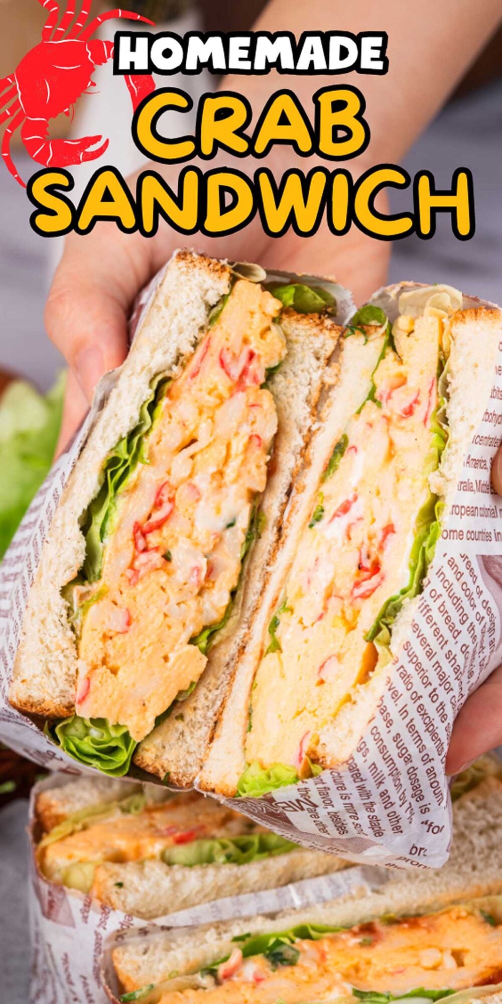A hand holds a halved Crab Sandwich with lettuce and creamy filling, wrapped in printed paper.