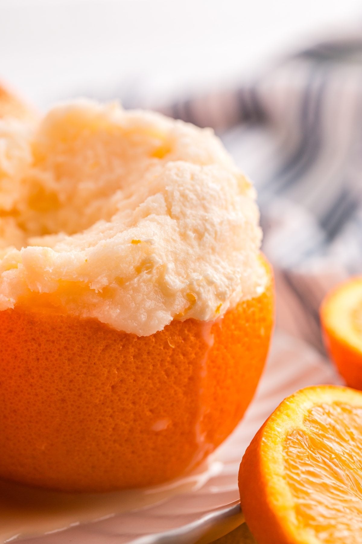A hollowed orange filled with creamy orange sorbet, with orange slices beside it on a white surface.