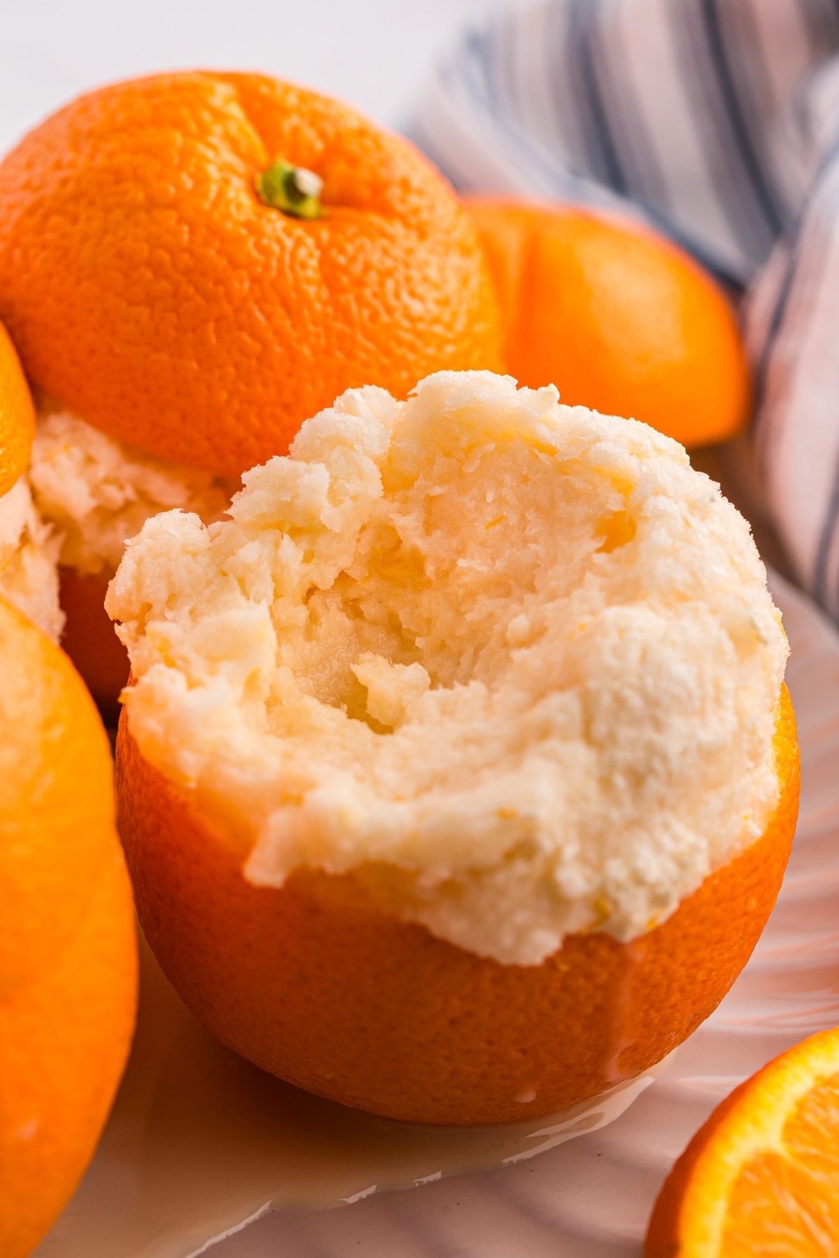 An orange half filled with creamy orange sorbet sits in front, with whole oranges arranged in the background.