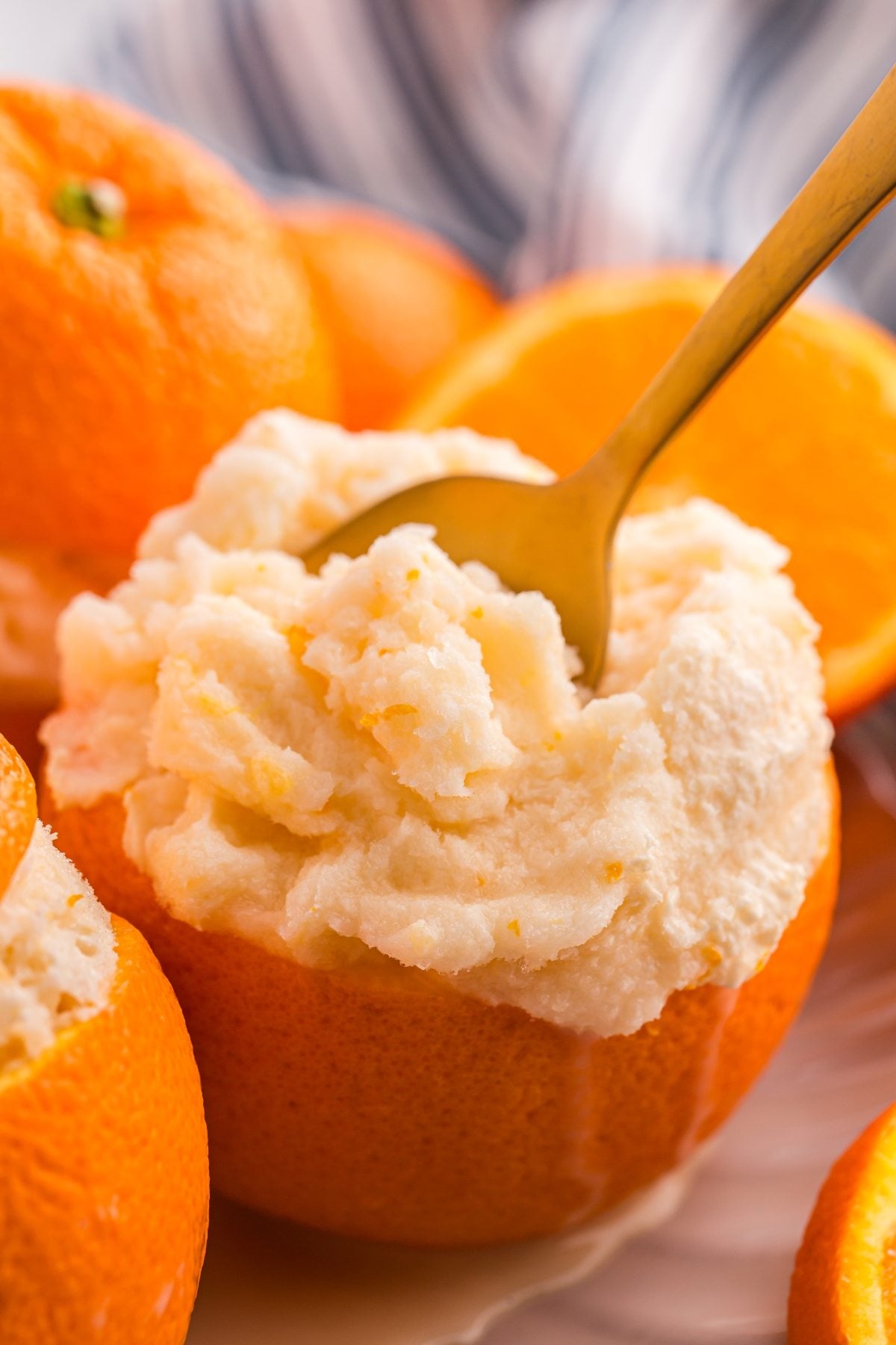A spoon scoops creamy orange sorbet served in a hollowed-out orange half.