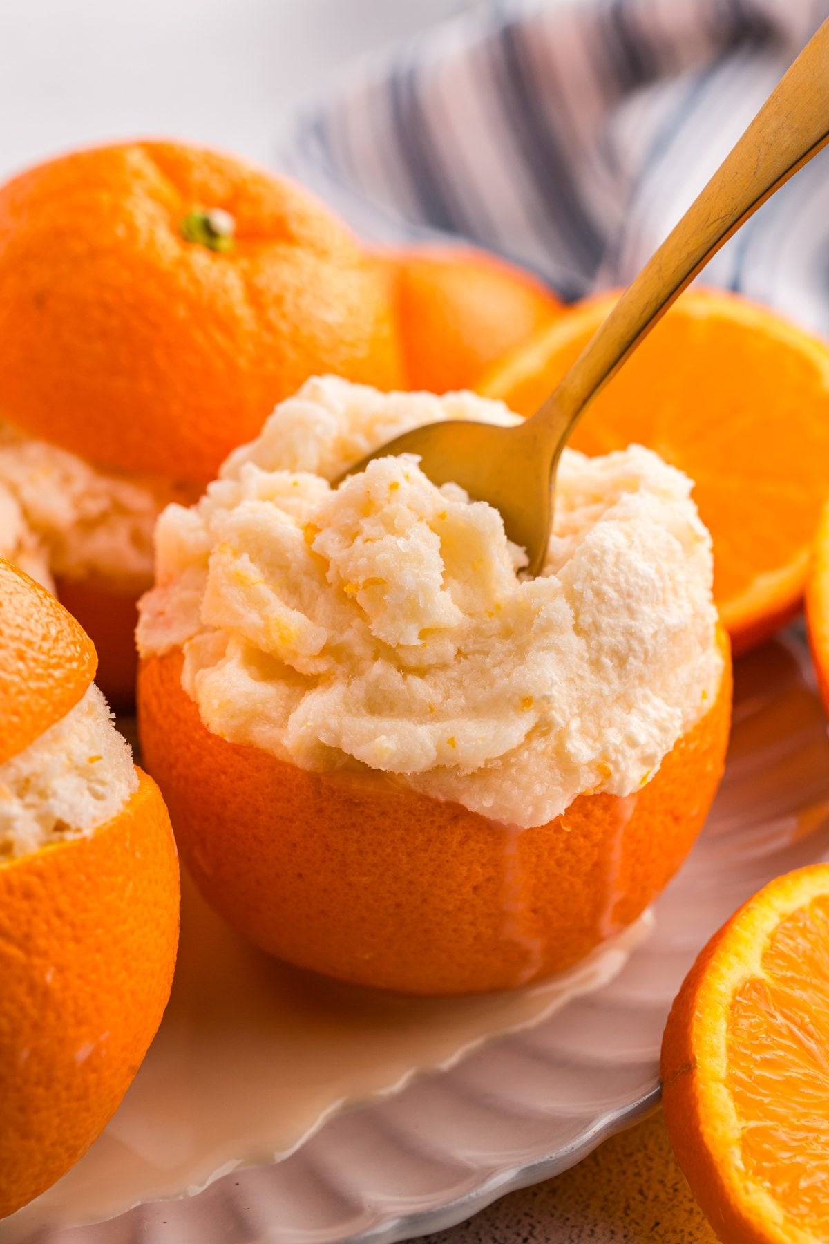 A hollowed orange filled with creamy orange sorbet, with a spoon scooping some out. Orange slices nearby.