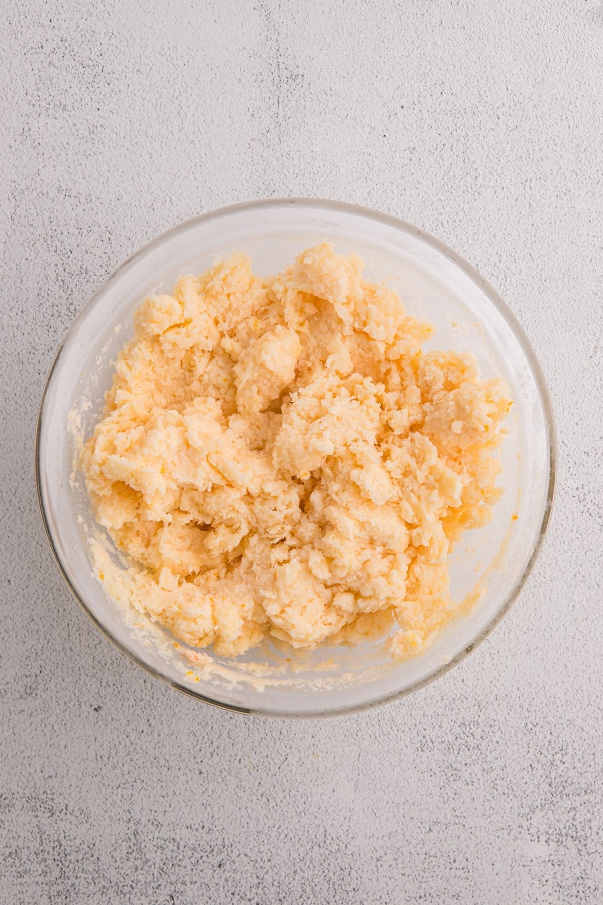 A glass bowl filled with pale, crumbly cookie dough sits on a light textured surface, evoking the refreshing hue of orange sorbet.