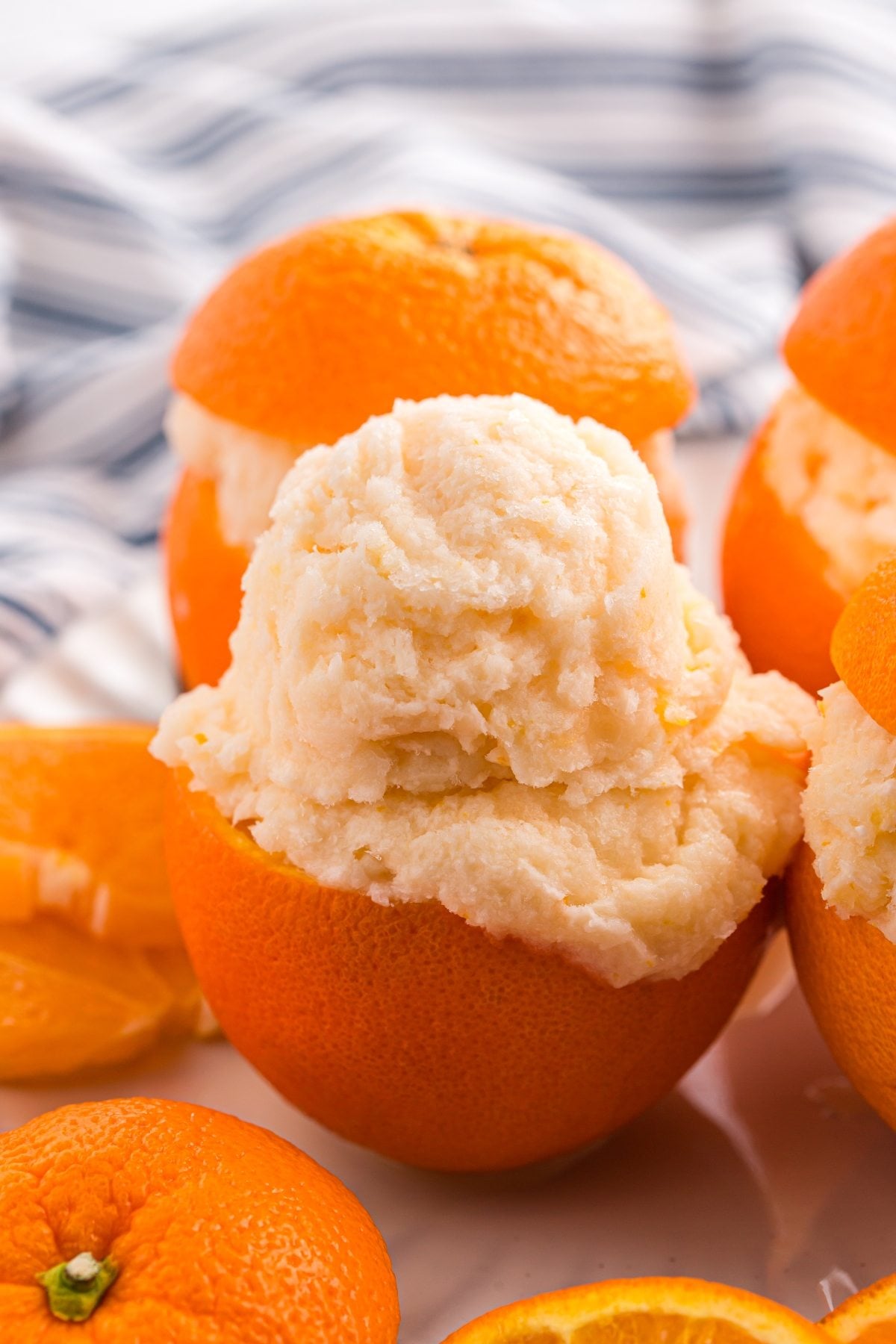 Orange sorbet served inside a hollowed-out orange, with extra orange slices and a striped cloth adding a fresh touch in the background.