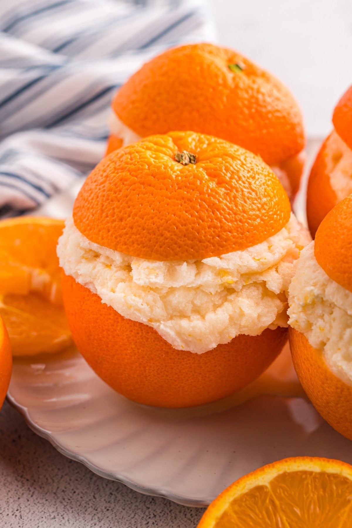 An orange with its top cut off, filled with creamy orange sorbet, sits on a white plate.