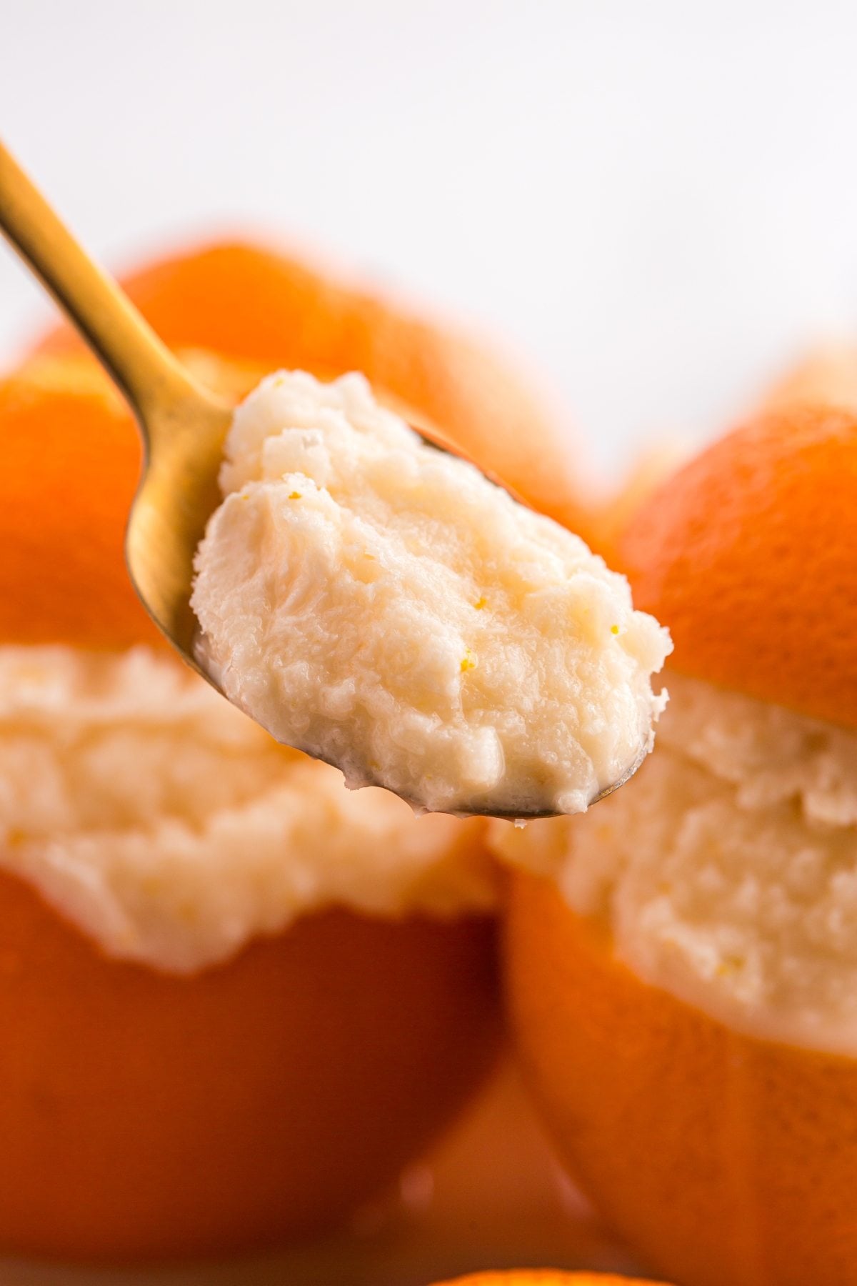 A spoon holding creamy orange sorbet with whole oranges filled with the same refreshing dessert in the background.