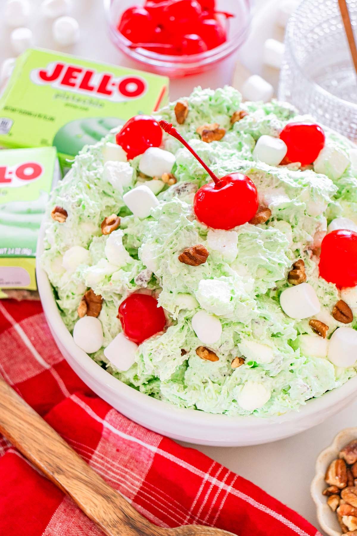 A bowl of classic Watergate Salad&mdash;green pistachio salad topped with marshmallows, pecans, and cherries&mdash;sits beside colorful Jell-O boxes.