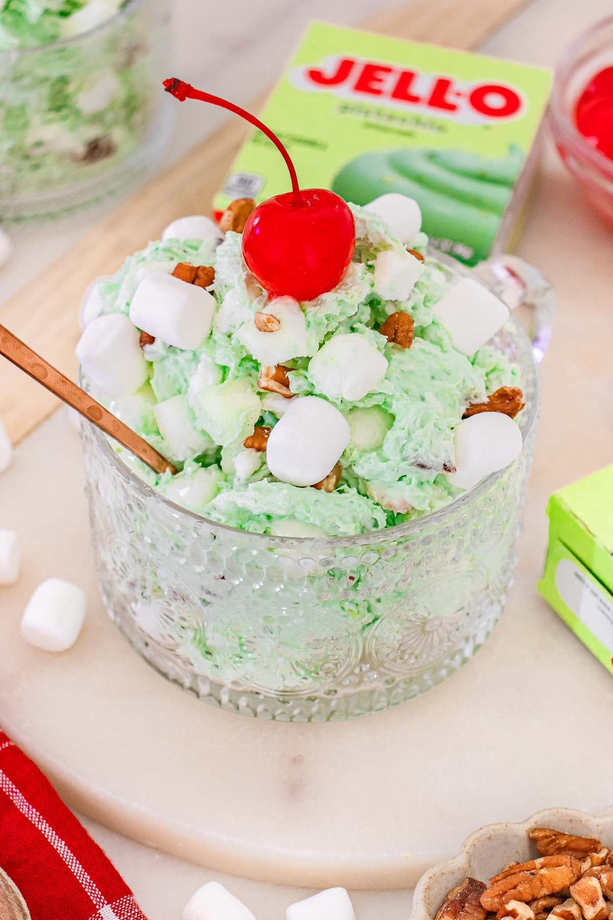 A glass bowl of classic Watergate Salad, green pistachio fluff topped with marshmallows, pecans, and a cherry.