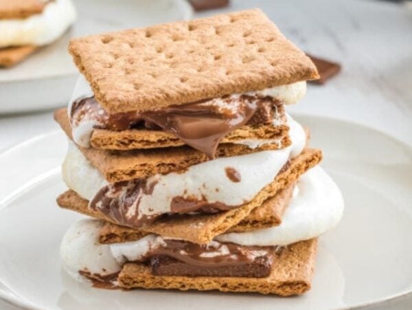 Stacked s'mores with melted chocolate and toasted marshmallows on a white plate—these easy treats are perfect for year-round desserts.