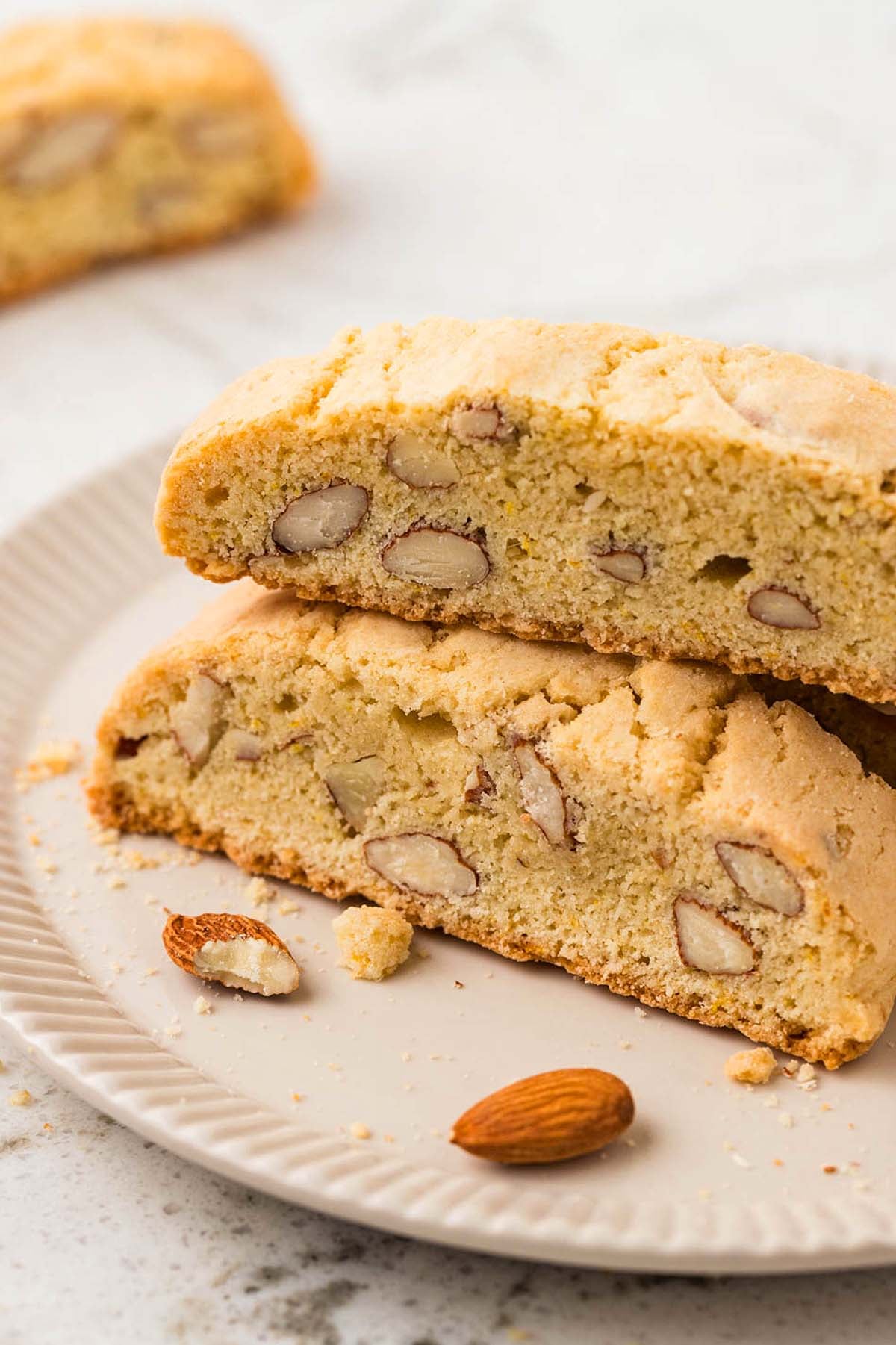 Two slices of almond biscotti rest on a plate, with whole almonds scattered nearby for an irresistible Almond Biscotti treat.