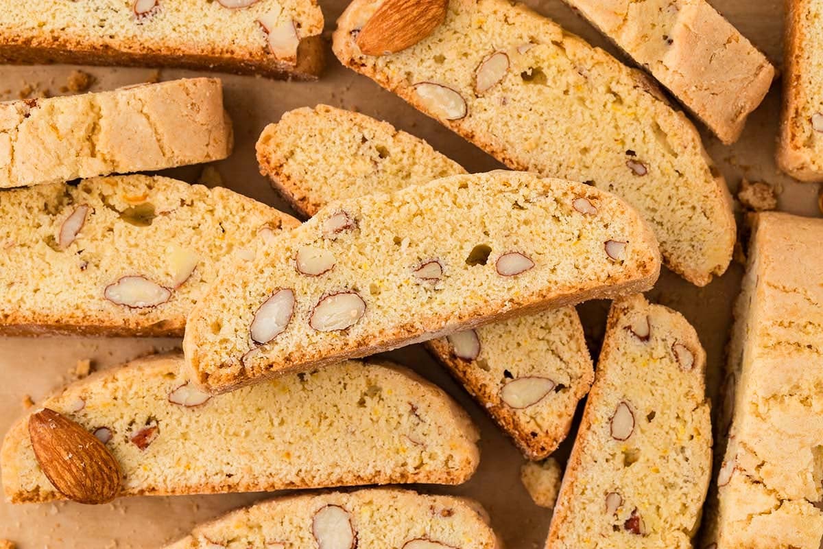 Almond Biscotti cookies arranged on a brown surface, with whole almonds visible inside and around the Almond Biscotti treats.