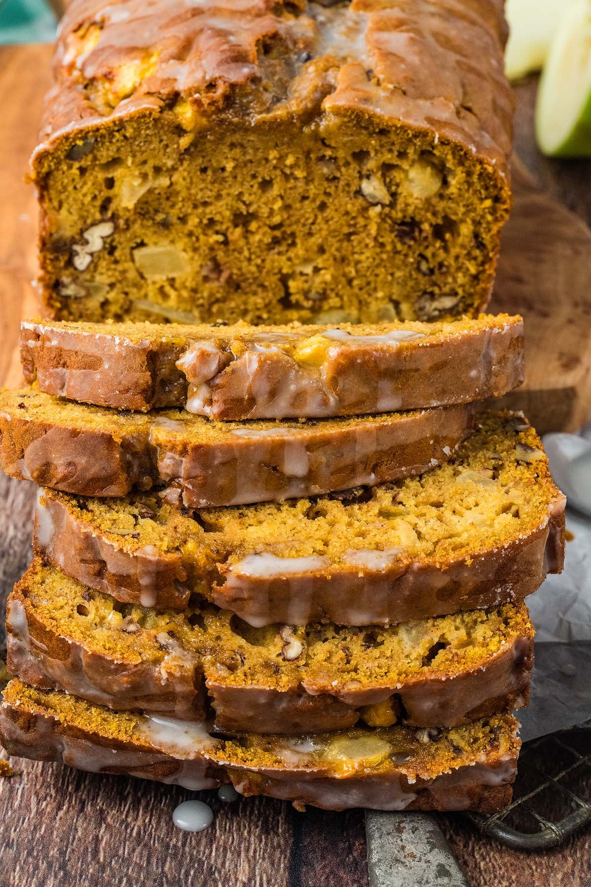 Sliced glazed apple pumpkin bread with nuts on a wooden board, showing a moist, golden interior.