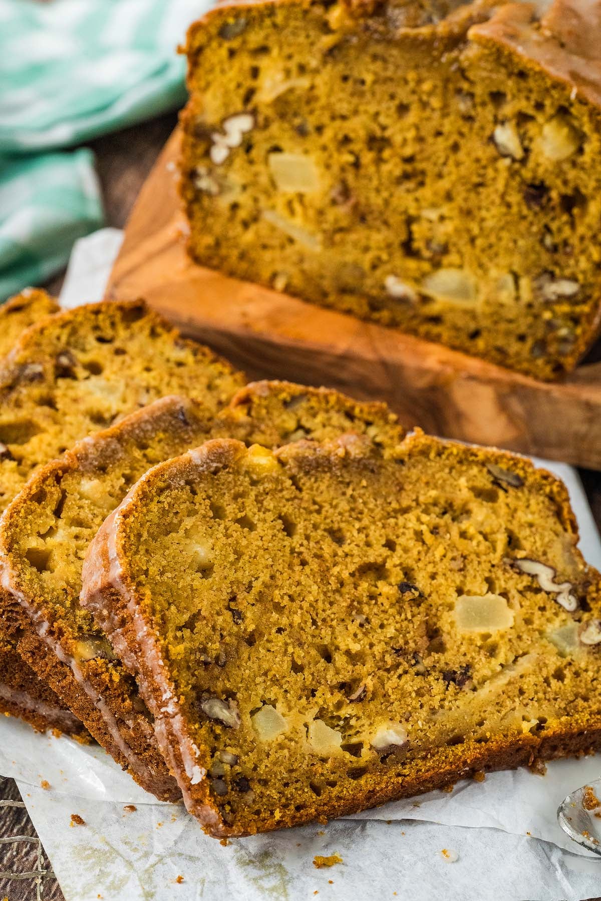 Sliced loaf of moist apple pumpkin bread with visible nuts and apple chunks on a parchment-lined surface.