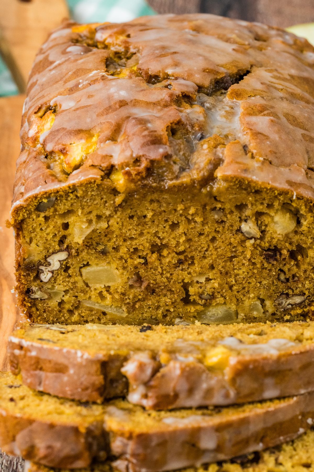 Close-up of a sliced loaf of glazed pumpkin bread with nuts and apple chunks inside.