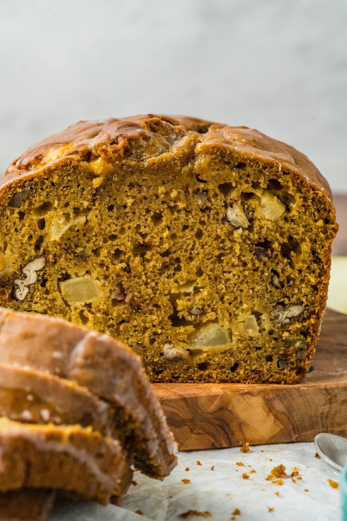 Close-up of sliced pumpkin bread with visible chunks of nuts and fruit on a wooden cutting board.