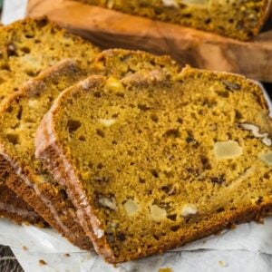 Slices of apple pumpkin bread with nuts and apple chunks rest on parchment paper, with a blue bowl in the background.