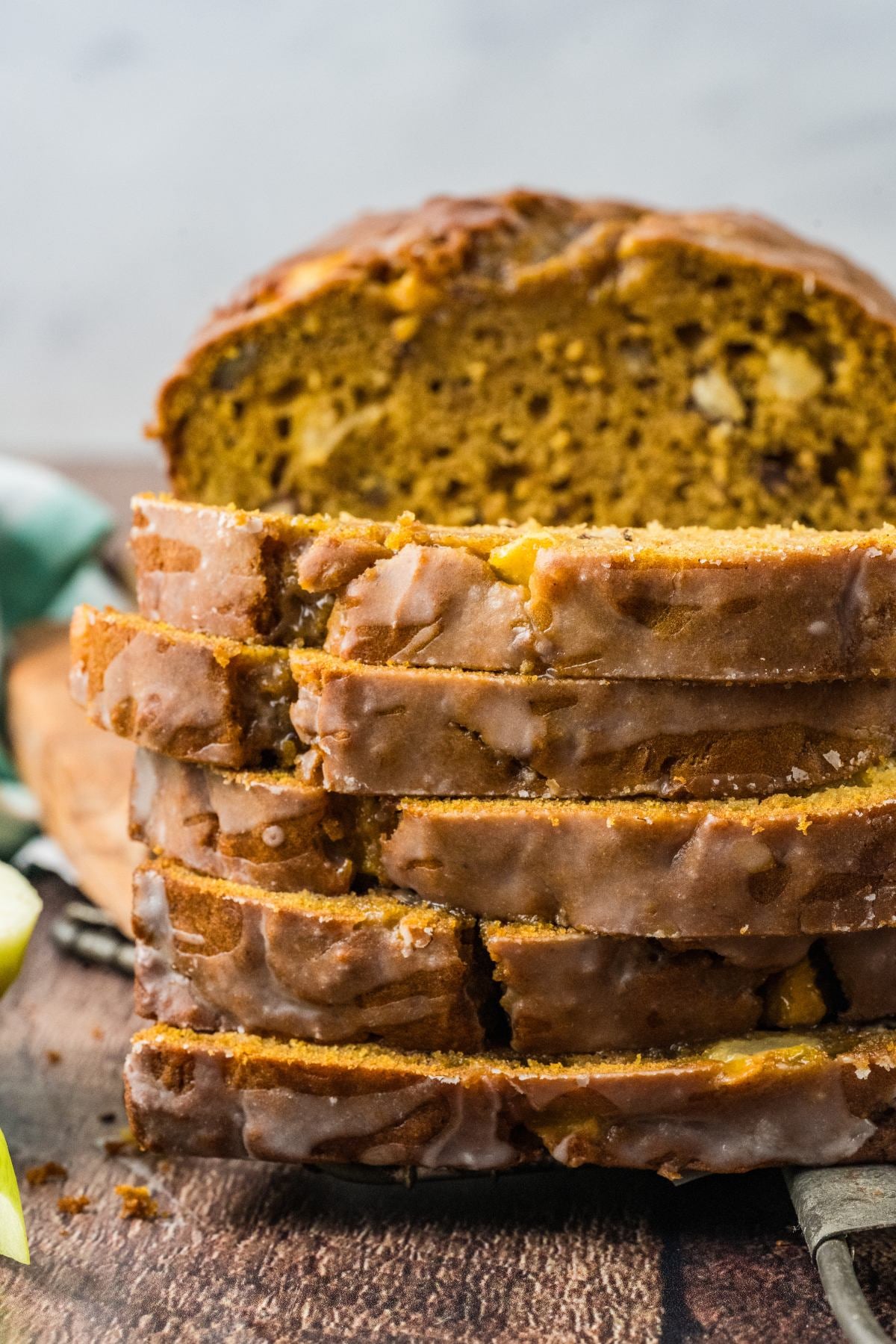 Sliced glazed pumpkin bread with nuts on a wooden surface, with a loaf in the background.