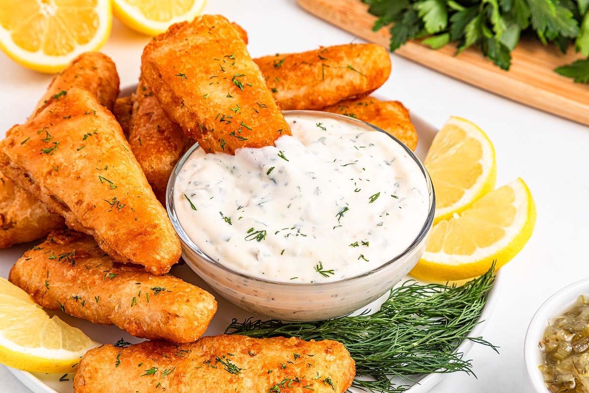 Golden fried fish fillets served with an easy tartar sauce, garnished with fresh dill and lemon wedges on a white plate.