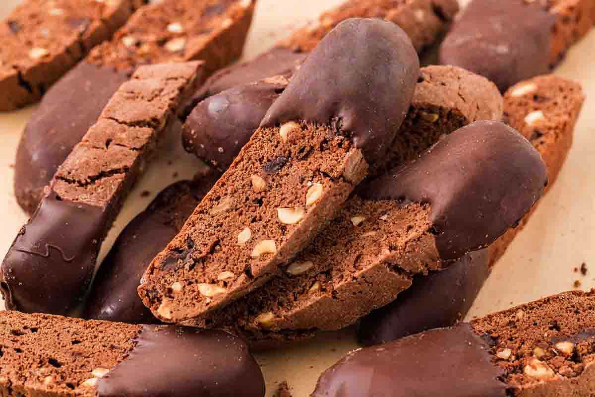 Chocolate biscotti with nuts, some pieces partially dipped in chocolate, are stacked closely together for an irresistible chocolate biscotti treat.
