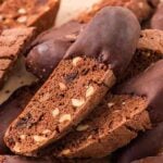Chocolate biscotti with nuts, some partially dipped in chocolate, are stacked on a light-colored surface for a tempting display of chocolate biscotti delight.