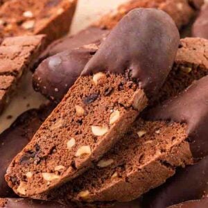 Chocolate biscotti with nuts, some partially dipped in chocolate, are stacked on a light-colored surface for a tempting display of chocolate biscotti delight.
