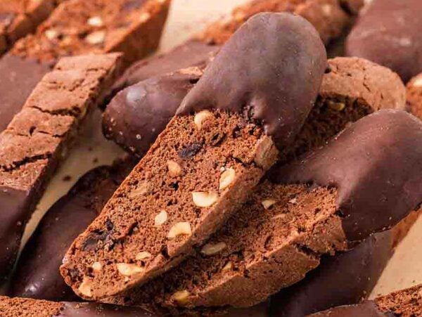 Chocolate biscotti with nuts, some partially dipped in chocolate, are stacked on a light-colored surface for a tempting display of chocolate biscotti delight.