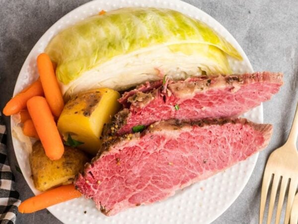 Plate with sliced corned beef, steamed cabbage, carrots, and potatoes next to a fork and knife set—a classic choice for those seeking delicious Corned Beef Recipes.