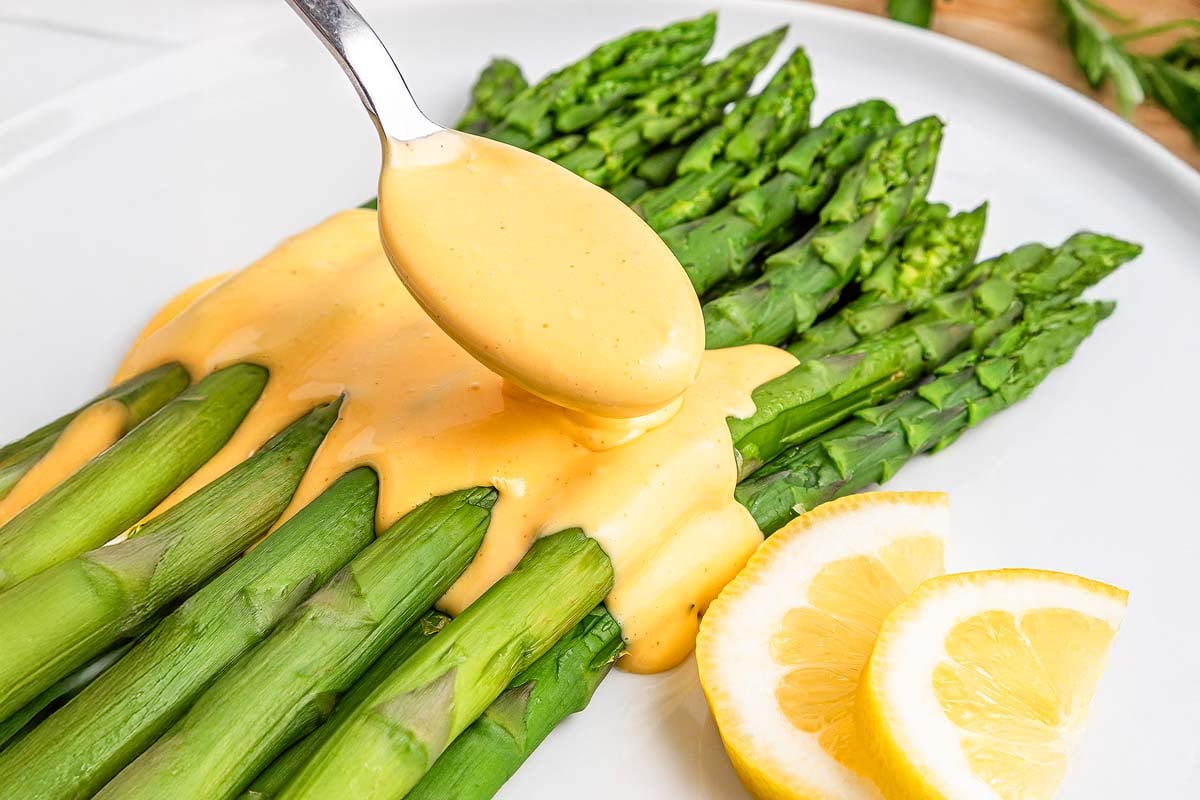 Steamed asparagus spears topped with easy hollandaise sauce, garnished with lemon slices on a white plate.