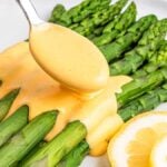 Fresh asparagus spears topped with easy Hollandaise sauce, garnished with lemon slices on a white plate.