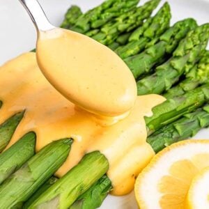 Fresh asparagus spears topped with easy Hollandaise sauce, garnished with lemon slices on a white plate.