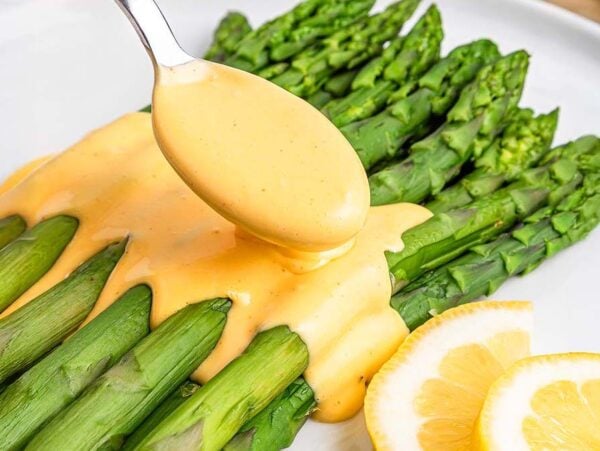 Fresh asparagus spears topped with easy Hollandaise sauce, garnished with lemon slices on a white plate.