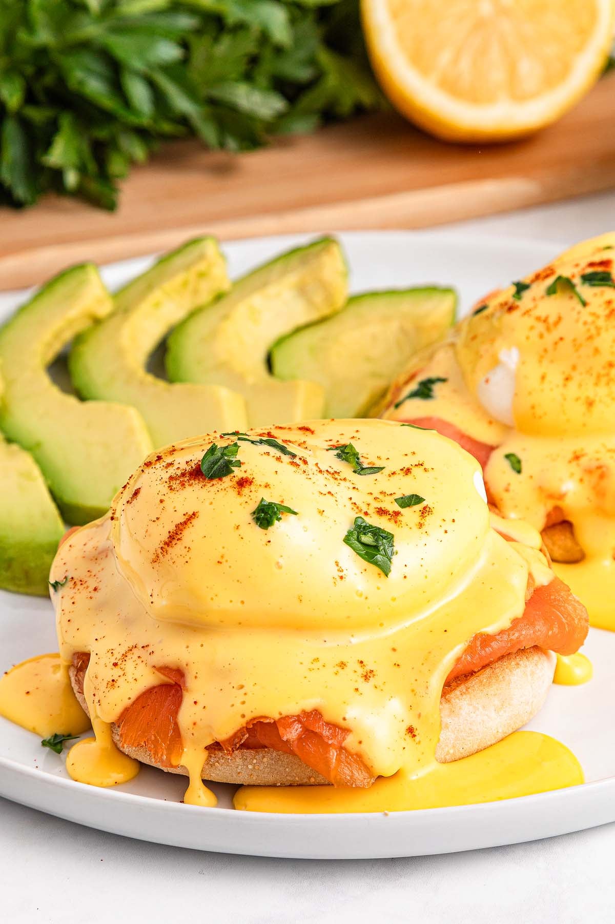 Smoked Salmon Eggs Benedict topped with creamy hollandaise sauce and fresh avocado slices, served on a white plate.