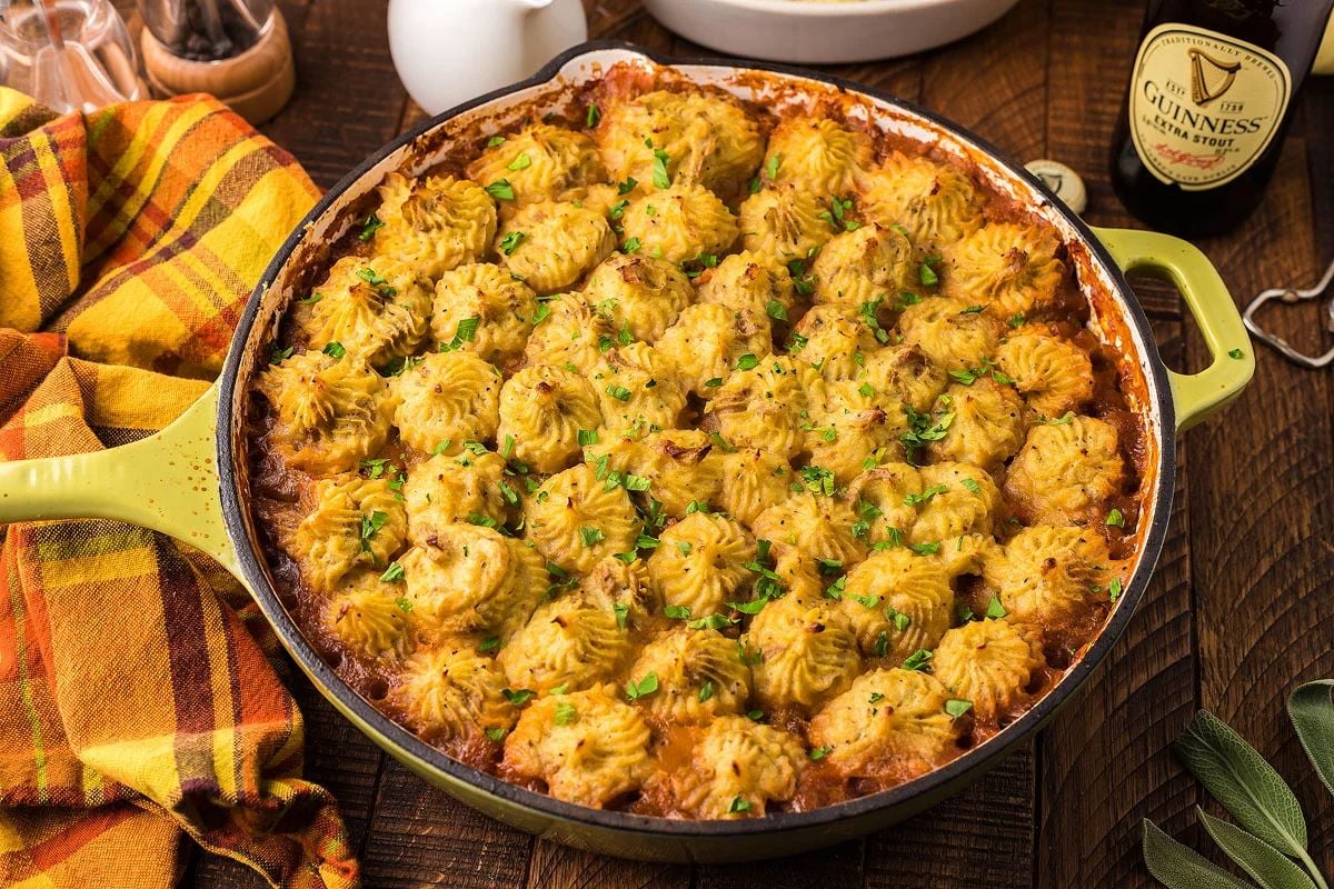 Shepherd’s pie with piped mashed potato topping in a green baking dish, enriched with Guinness cooking and garnished with herbs.