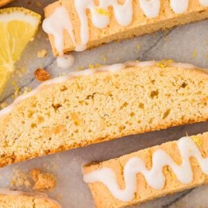 Lemon biscotti with white icing drizzle and fresh lemon slices arranged on a marble surface create a zesty, elegant treat.