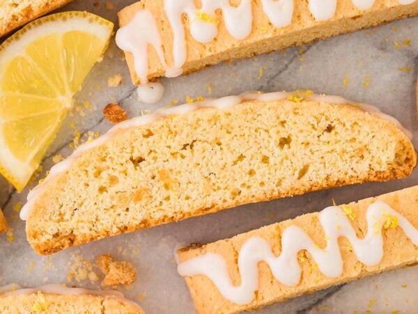 Lemon biscotti with white icing drizzle and fresh lemon slices arranged on a marble surface create a zesty, elegant treat.