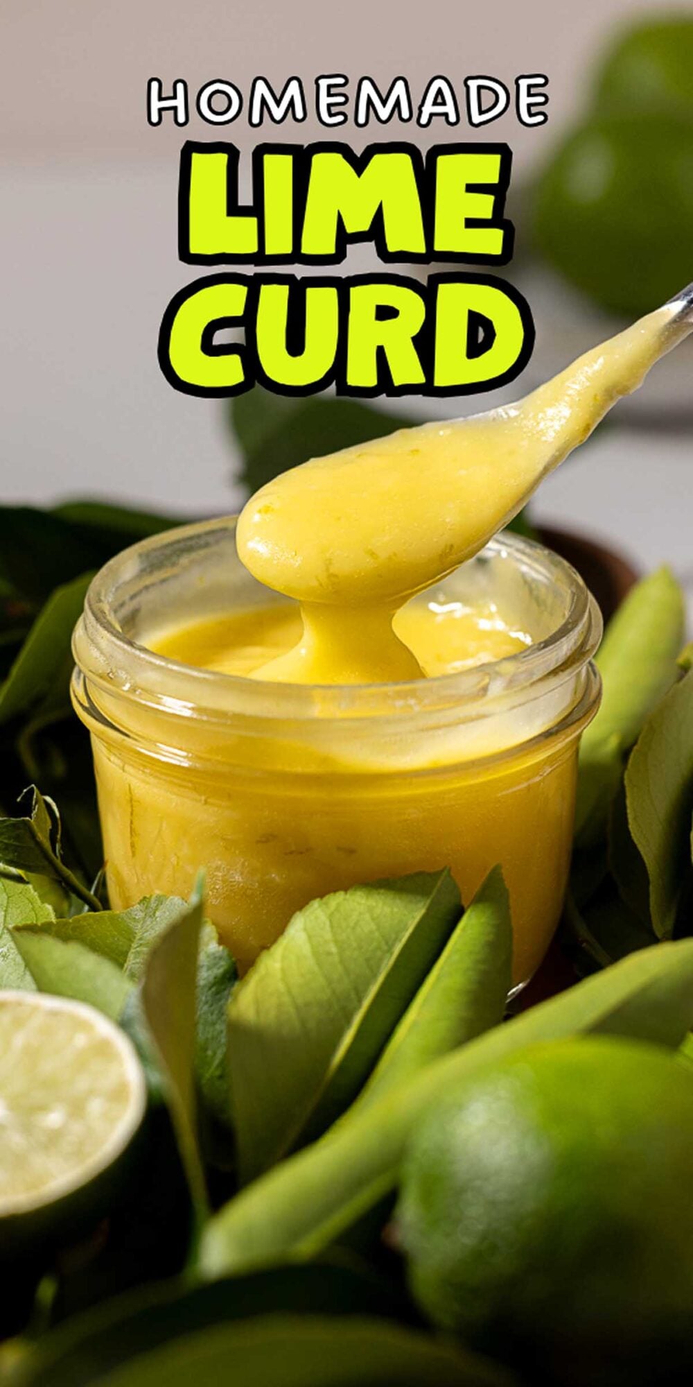 A spoon scoops vibrant lime curd from a jar, surrounded by fresh limes and green leaves.