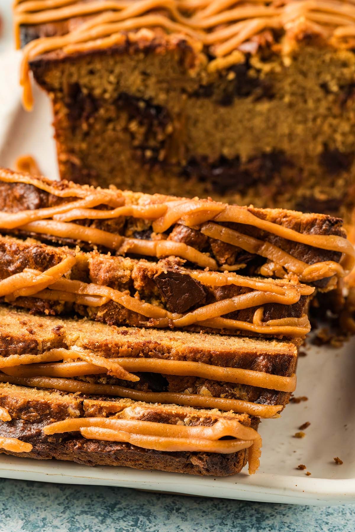 Sliced chocolate chip loaf drizzled with caramel icing on a white plate, reminiscent of classic Peanut Butter Banana Bread flavors.