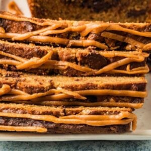 Slices of Peanut Butter Banana Bread drizzled with caramel icing, stacked on a white plate.