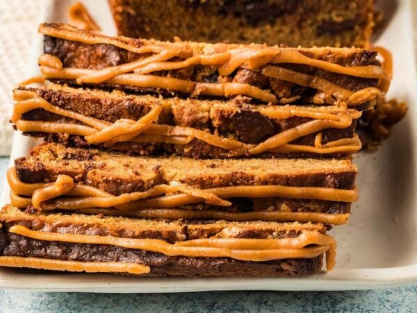 Slices of Peanut Butter Banana Bread drizzled with caramel icing, stacked on a white plate.