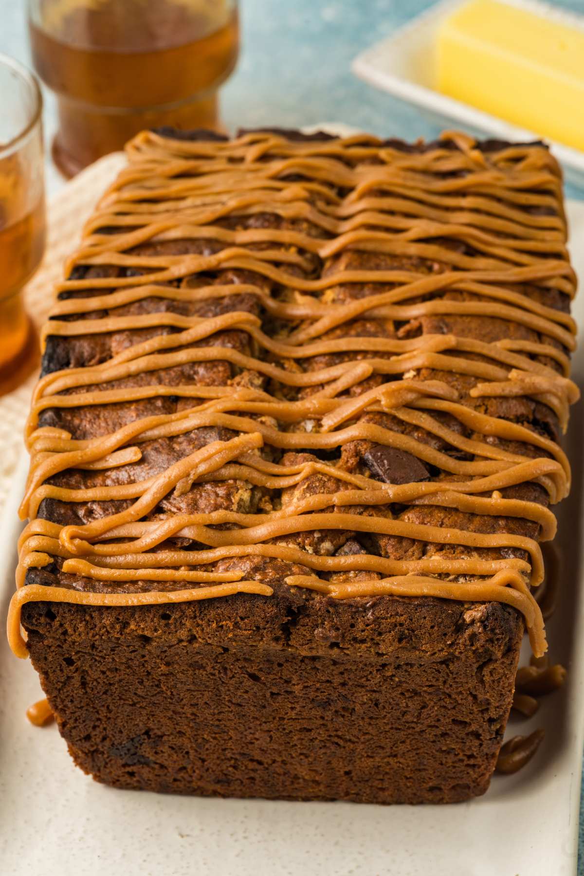 A loaf of banana bread topped with a thick drizzle of caramel icing on a white plate.