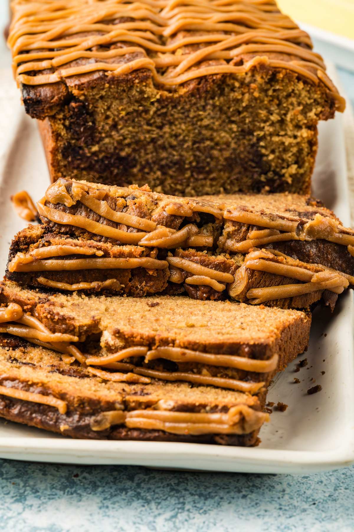 Close-up of sliced loaf cake with caramel or peanut butter drizzle on top, arranged on a white tray.