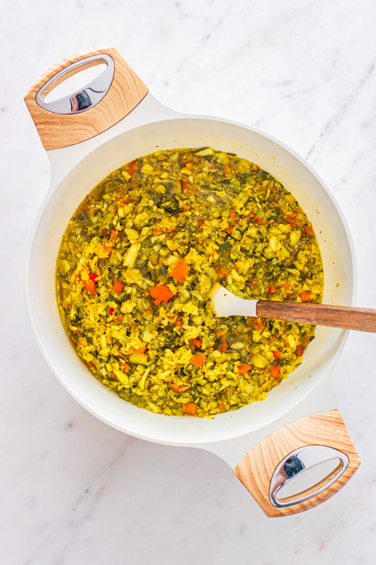 A white pot filled with chopped vegetables and broth, with a wooden spoon resting inside.