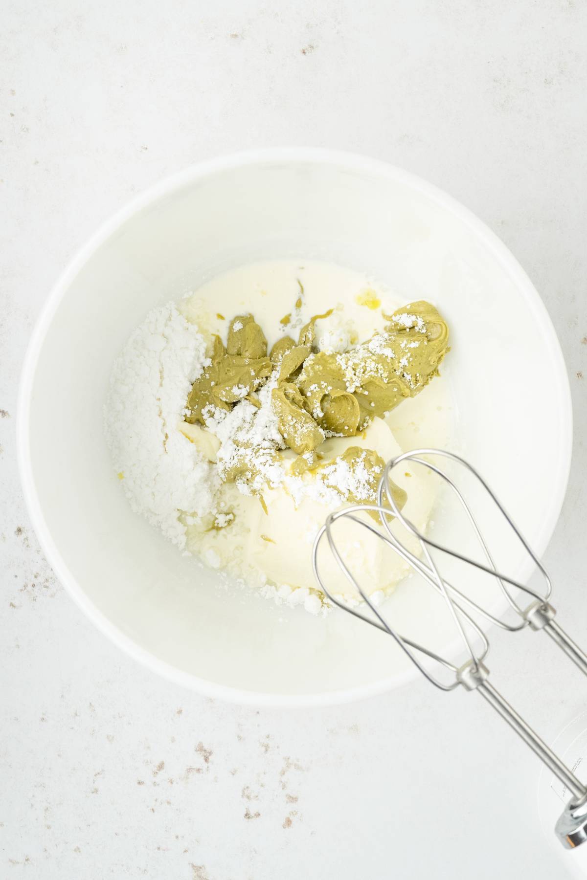 A round pistachio ricotta cake with green frosting, chopped pistachios, and a white icing swirl sits on a plate with cutlery nearby.