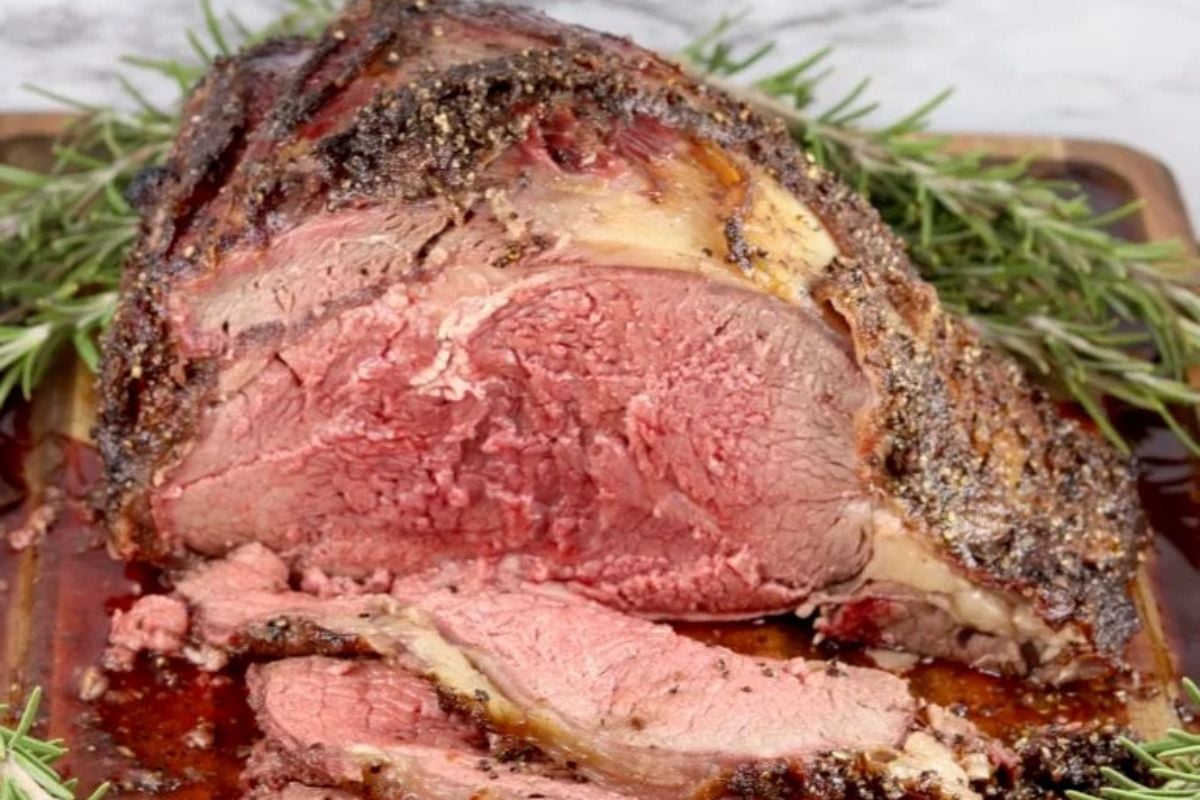 Sliced medium rare roast beef with a seasoned crust, garnished with fresh rosemary on a wooden board—perfect for holiday main course recipes.