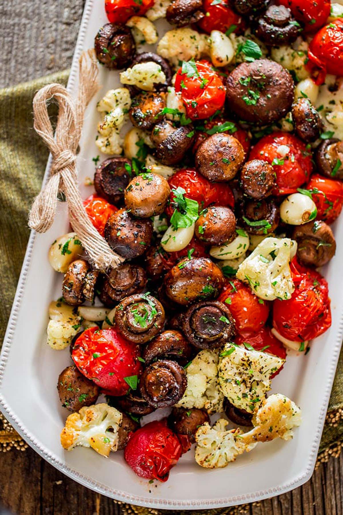 Roasted mushrooms, tomatoes, cauliflower, and garlic garnished with herbs on a white platter—perfect for those seeking Vegan Italian Recipes.